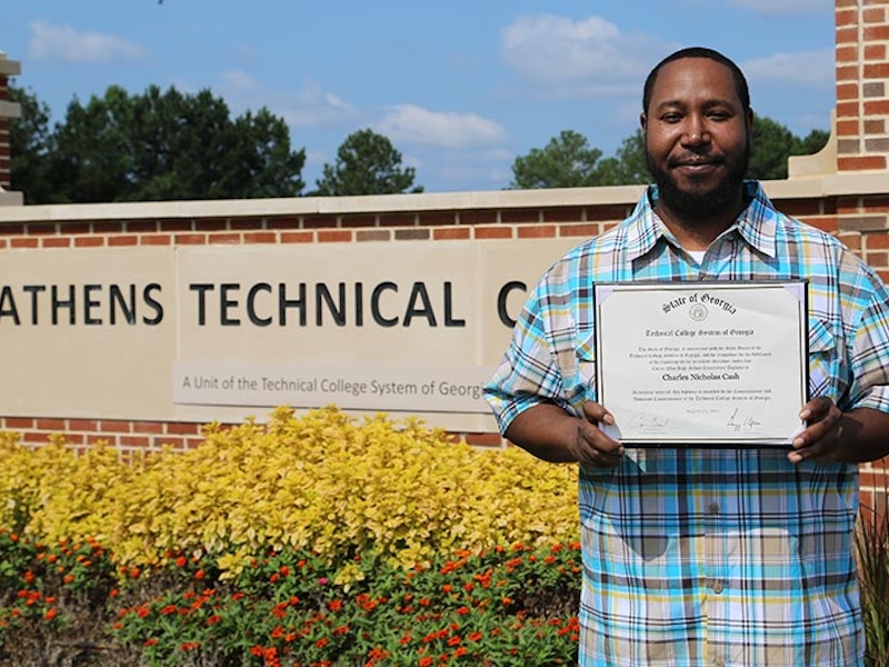 Man holding diploma in front of Athens Tech signage